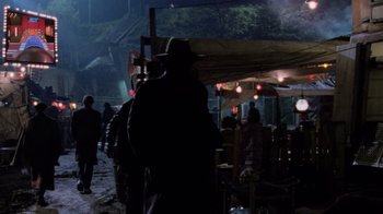 Movie still from “The Running Man” (1987), directed by Paul Michael Glaser – A group of people standing in a dark room; Wide shot, High angle