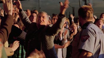 Movie still from “The Running Man” (1987), directed by Paul Michael Glaser – A group of people standing in a crowd with their hands in the air; Medium shot, High angle