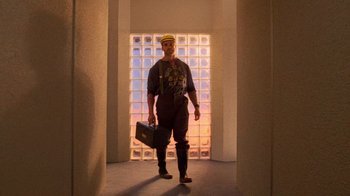 Movie still from “The Running Man” (1987), directed by Paul Michael Glaser – A man holding a briefcase while standing in front of a window; Wide shot, Low angle