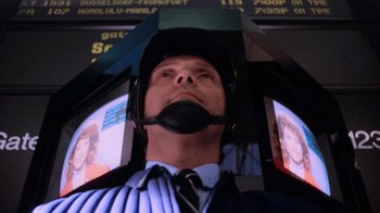 Movie still from “The Running Man” (1987), directed by Paul Michael Glaser – A man in a suit and tie with an umbrella; Close Up shot, Low angle