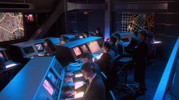 Movie still from “The Running Man” (1987), directed by Paul Michael Glaser – A group of people sitting at computers in a dark room; Wide shot, High angle