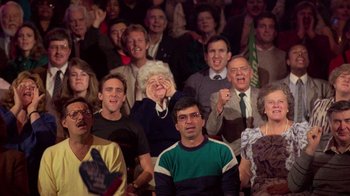 Movie still from “The Running Man” (1987), directed by Paul Michael Glaser – A group of people sitting in front of each other; Medium shot, High angle
