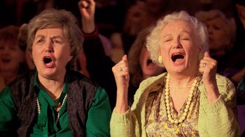 Movie still from “The Running Man” (1987), directed by Paul Michael Glaser – Two older women singing in front of an audience; Close Up shot, Low angle