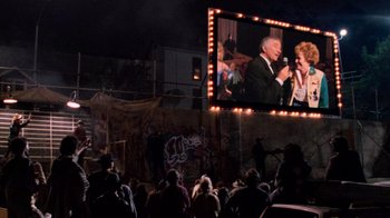 Movie still from “The Running Man” (1987), directed by Paul Michael Glaser – People watching a movie on a big screen; Wide shot, Over the shoulder angle