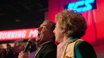 Movie still from “The Running Man” (1987), directed by Paul Michael Glaser – A man and a woman singing into a microphone; Close Up shot, Low angle