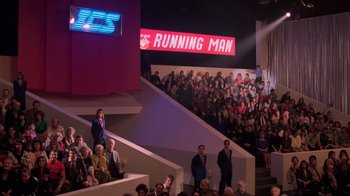 Movie still from “The Running Man” (1987), directed by Paul Michael Glaser – A group of people standing in front of a crowd; Extreme Wide shot, High angle
