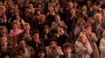 Movie still from “The Running Man” (1987), directed by Paul Michael Glaser – A group of people sitting in a room clapping and applauding; Wide shot, High angle
