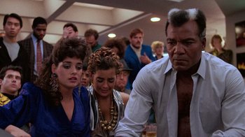 Movie still from “The Running Man” (1987), directed by Paul Michael Glaser – A group of people sitting in front of a group of other people; Medium shot, Over the shoulder angle