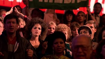 Movie still from “The Running Man” (1987), directed by Paul Michael Glaser – A group of people standing in a room; Medium shot, Over the shoulder angle