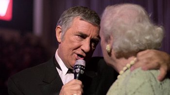 Movie still from “The Running Man” (1987), directed by Paul Michael Glaser – An older man in a tuxedo is talking to an older woman; Close Up shot, Over the shoulder angle