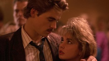 Movie still from “The Running Man” (1987), directed by Paul Michael Glaser – A man and a woman standing next to each other; Close Up shot, Over the shoulder angle