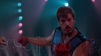 Movie still from “The Running Man” (1987), directed by Paul Michael Glaser – A man wearing boxing gloves and posing for a picture; Close Up shot, Low angle