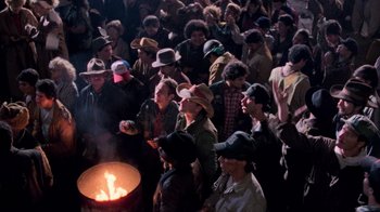 Movie still from “The Running Man” (1987), directed by Paul Michael Glaser – A group of people standing in front of an open fire; Wide shot, High angle