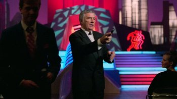 Movie still from “The Running Man” (1987), directed by Paul Michael Glaser – A man in a suit and tie holding a remote control; Medium shot, Low angle