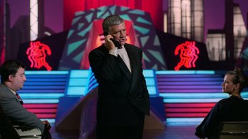 Movie still from “The Running Man” (1987), directed by Paul Michael Glaser – A man talking on a cell phone while standing in front of stage lights; Medium shot, Low angle