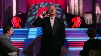 Movie still from “The Running Man” (1987), directed by Paul Michael Glaser – A man in a suit and tie talking on a cell phone; Medium shot, Low angle