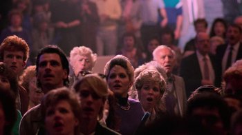 Movie still from “The Running Man” (1987), directed by Paul Michael Glaser – A group of people that are sitting in a room; Medium shot, High angle