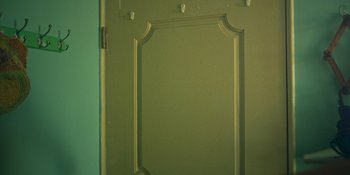Movie still from “The Sadness” (2021), directed by Rob Jabbaz – A green door with a white frame on the wall; Extreme Close Up shot, Overhead angle