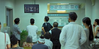 Movie still from “The Sadness” (2021), directed by Rob Jabbaz – A group of people standing in front of a television; Wide shot, Over the shoulder angle