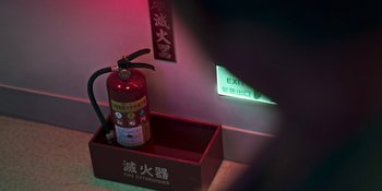 Movie still from “The Sadness” (2021), directed by Rob Jabbaz – A fire extinguisher is on display next to an exit sign; Extreme Close Up shot, High angle