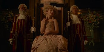 Movie still from “The School for Good and Evil” (2022), directed by Paul Feig – A woman in a pink dress is sitting in front of two other people; Medium shot, Low angle