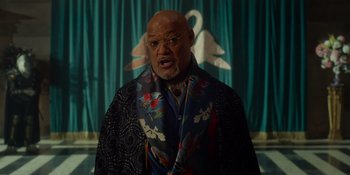 Movie still from “The School for Good and Evil” (2022), directed by Paul Feig – An older man wearing a colorful jacket in front of a curtain; Medium shot, Low angle