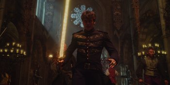 Movie still from “The School for Good and Evil” (2022), directed by Paul Feig – A man dressed in a uniform holding a sword in front of a stained glass window; Medium shot, Low angle