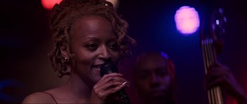 Movie still from “The Score” (2001), directed by Frank Oz – A woman is singing into a microphone in front of a group of people; Close Up shot, Over the shoulder angle