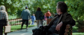 Movie still from “The Score” (2001), directed by Frank Oz – A man sitting on a park bench holding a camera; Medium shot, Over the shoulder angle