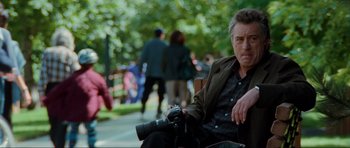 Movie still from “The Score” (2001), directed by Frank Oz – A man sitting on top of a bench with a camera; Medium shot, Over the shoulder angle