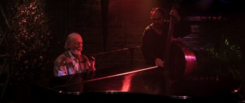 Movie still from “The Score” (2001), directed by Frank Oz – A man sitting at a piano in front of a microphone; Wide shot, Low angle