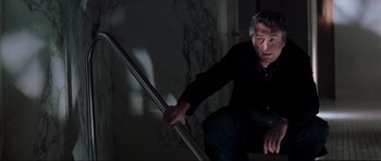 Movie still from “The Score” (2001), directed by Frank Oz – A man leaning on a metal railing in a dark room; Medium shot, Low angle