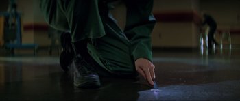 Movie still from “The Score” (2001), directed by Frank Oz – A person in green pants and black shoes writing on the floor; Extreme Close Up shot, High angle