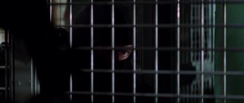 Movie still from “The Score” (2001), directed by Frank Oz – A person in a black mask behind a metal fence; Close Up shot, Low angle