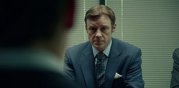 Movie still from “Dopesick” (2021), directed by Danny Strong – A man wearing a suit and tie sitting in front of a window; Close Up shot, Over the shoulder angle