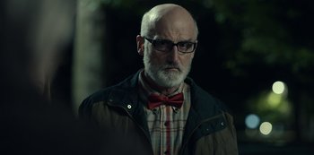 Movie still from “Dopesick” (2021), directed by Danny Strong – An older man wearing a bow tie and glasses; Close Up shot, Over the shoulder angle