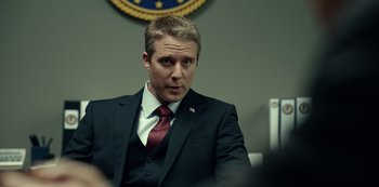 Movie still from “Dopesick” (2021), directed by Danny Strong – A man wearing a suit and tie sitting in front of a wall; Close Up shot, Over the shoulder angle