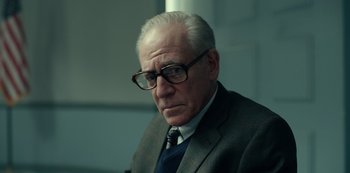 Movie still from “Dopesick” (2021), directed by Danny Strong – An older man wearing glasses and a suit; Close Up shot, Low angle