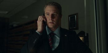 Movie still from “Dopesick” (2021), directed by Danny Strong – A man in a suit and tie talking on a cell phone; Medium shot, Low angle