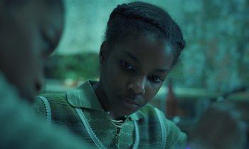 Movie still from “The Silent Twins” (2022), directed by Agnieszka Smoczynska – A young girl is looking at the camera; Close Up shot, Over the shoulder angle