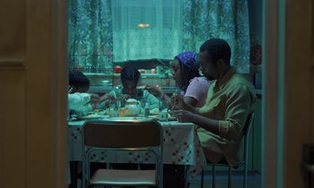 Movie still from “The Silent Twins” (2022), directed by Agnieszka Smoczynska – A group of people sitting at a table eating food; Wide shot, High angle