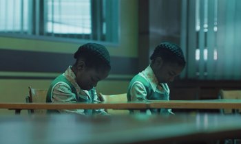 Movie still from “The Silent Twins” (2022), directed by Agnieszka Smoczynska – A couple of people that are sitting in a room; Medium shot, High angle