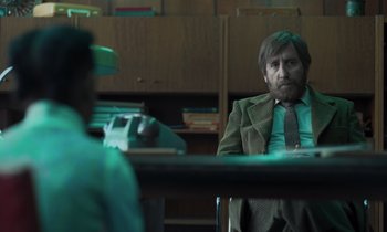 Movie still from “The Silent Twins” (2022), directed by Agnieszka Smoczynska – A man sitting at a desk in front of a typewriter; Medium shot, Over the shoulder angle