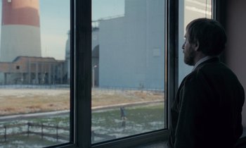 Movie still from “The Silent Twins” (2022), directed by Agnieszka Smoczynska – A man looking out of a window at a field; Medium shot, Over the shoulder angle