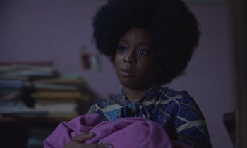 Movie still from “The Silent Twins” (2022), directed by Agnieszka Smoczynska – A woman with a large afro holding a pink blanket; Close Up shot, Over the shoulder angle