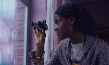 Movie still from “The Silent Twins” (2022), directed by Agnieszka Smoczynska – A person holding a video camera up to their face; Close Up shot, Low angle