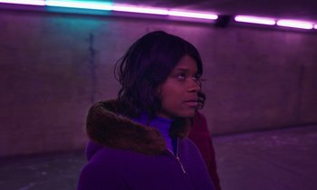 Movie still from “The Silent Twins” (2022), directed by Agnieszka Smoczynska – A woman in a purple jacket and a purple jacket; Medium shot, Low angle