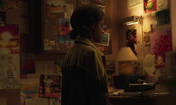 Movie still from “The Silent Twins” (2022), directed by Agnieszka Smoczynska – A person standing in a room with a lamp on; Medium shot, Over the shoulder angle
