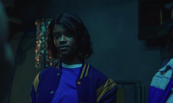 Movie still from “The Silent Twins” (2022), directed by Agnieszka Smoczynska – A man with long hair wearing a blue and yellow jacket; Close Up shot, Low angle