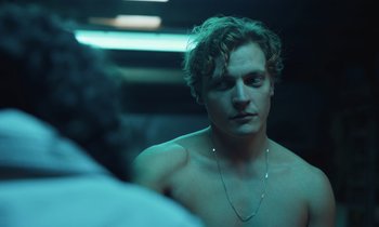 Movie still from “The Silent Twins” (2022), directed by Agnieszka Smoczynska – A young man with a necklace is looking into a mirror; Close Up shot, Over the shoulder angle